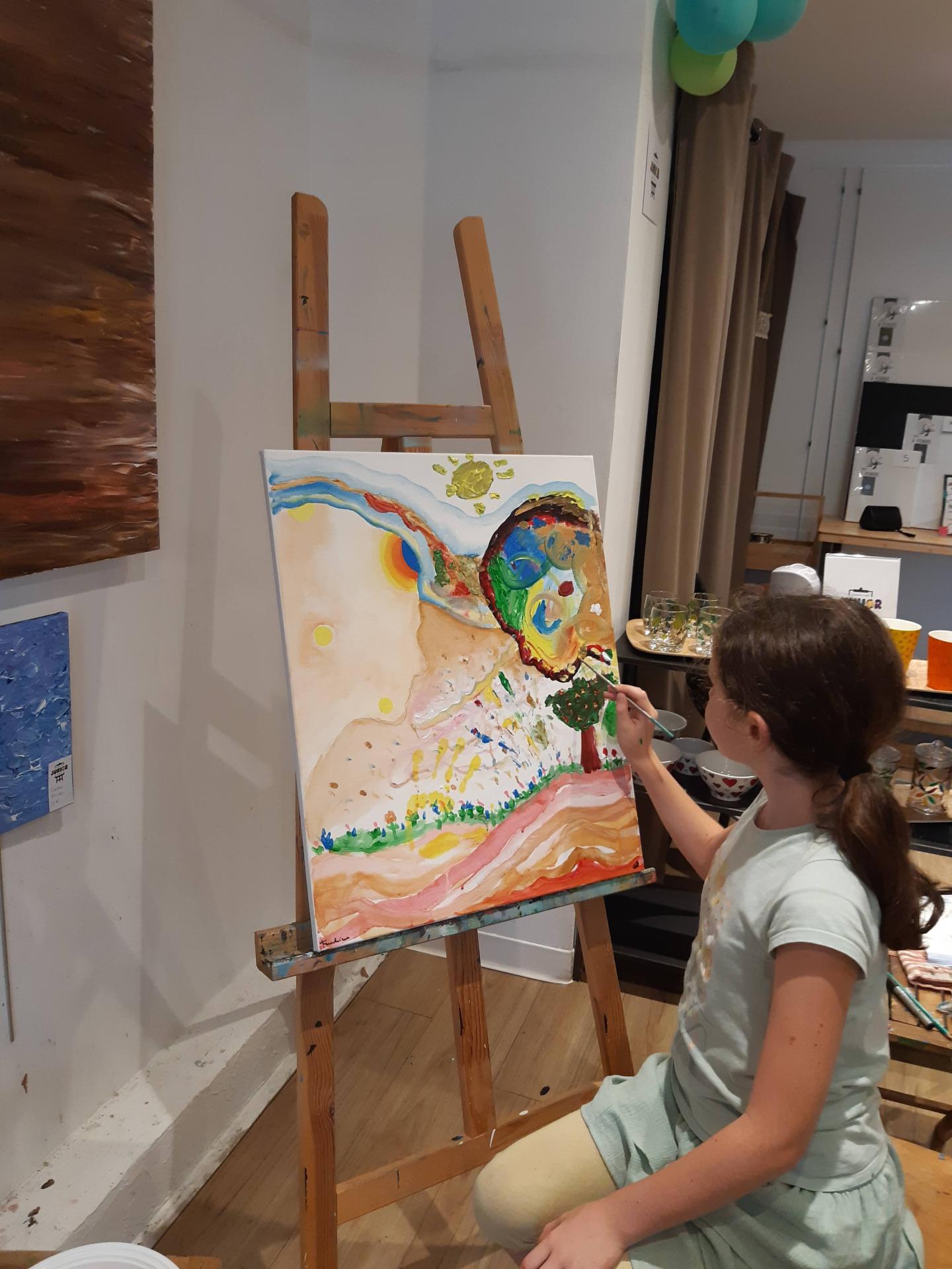 Une enfant peint debout devant son chevalet pendant un atelier